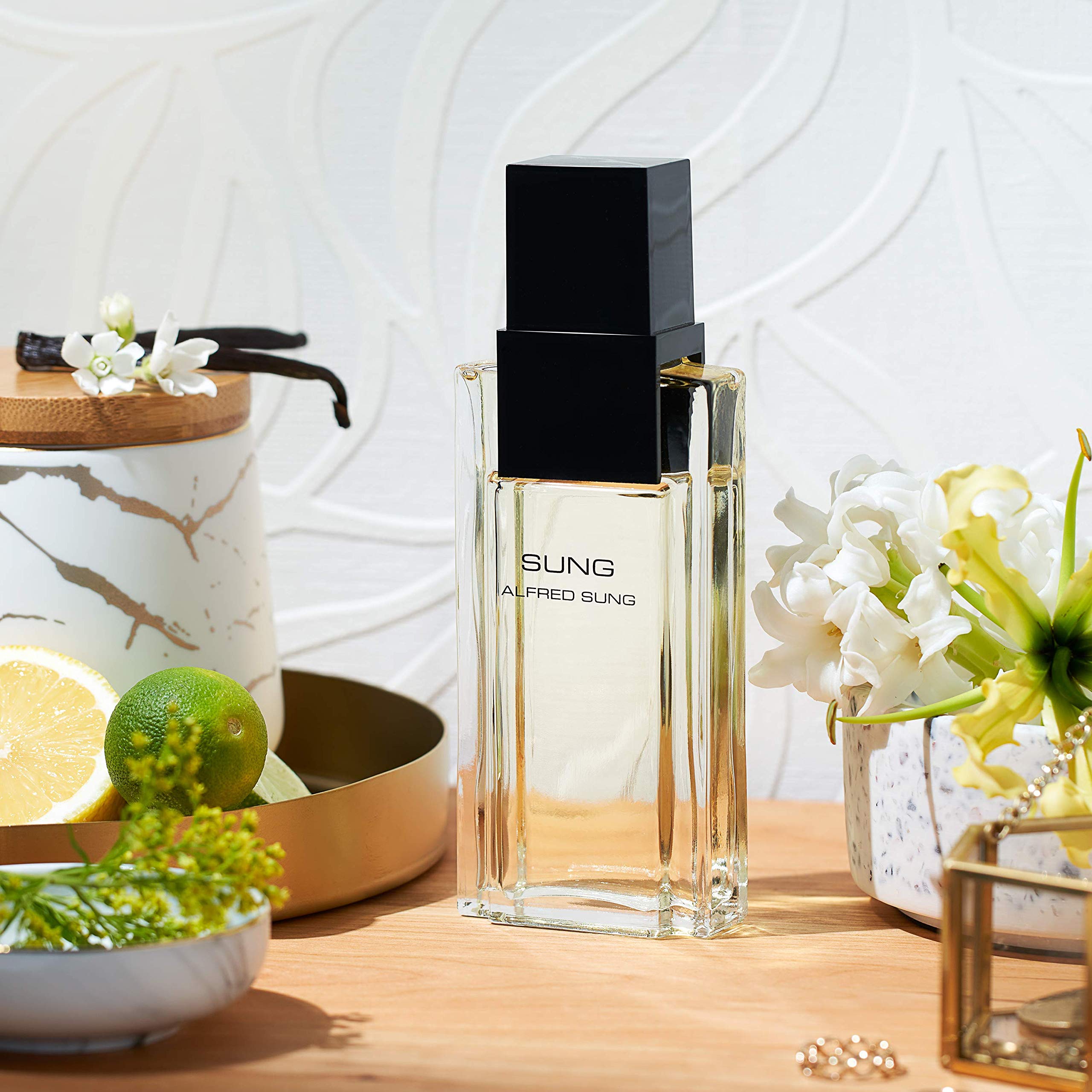 ALFRED SUNG bottle beside white flowers and citrus showing scent notes benefit: floral-citrus clarity