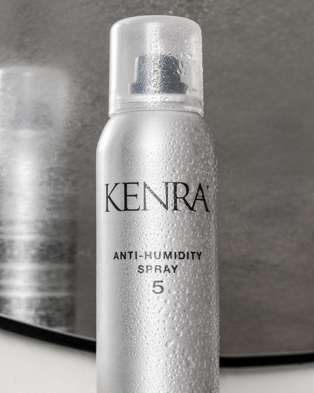 Kenra bottle beside hand showing 5oz scale and travel-friendly benefit