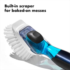 OXO view of scraper on brush backside lifting baked-on food without scratching pans